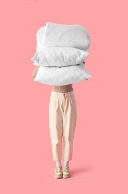 Beyaz yastıklı ve pembe arka planda katlanmış battaniyeli kadın.