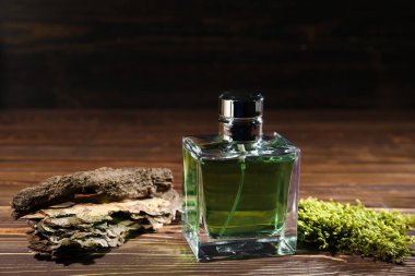 Yeşil erkek parfüm şişesi ve ahşap masada dekoratif yosun.