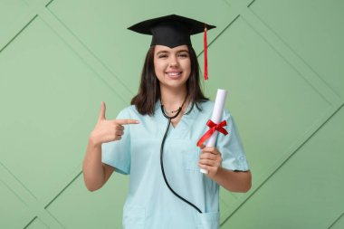 Mezuniyet şapkalı mutlu bayan tıp öğrencisi yeşil ahşap arka plan diplomasını gösteriyor.