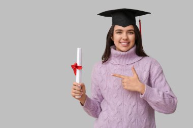 Mezuniyet şapkalı mutlu bayan öğrenci beyaz arka plandaki diplomayı gösteriyor.