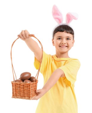 Beyaz arka planda Paskalya için çikolatalı yumurta sepeti tutan tavşan kulaklı şirin bir çocuk.