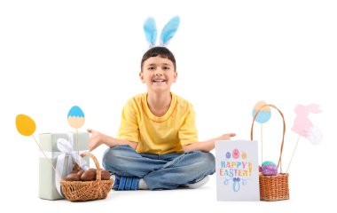 Tavşan kulaklı şirin bir çocuk. Beyaz arka planda çikolata yumurtası sepeti, hediye kutusu ve Paskalya için dekor var.