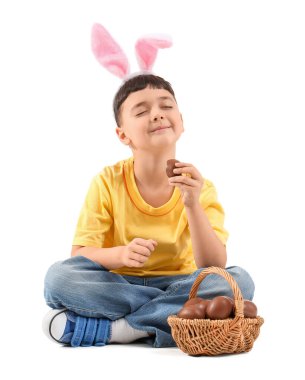 Beyaz arka planda Paskalya için çikolata yumurtalı tavşan kulaklı şirin bir çocuk.