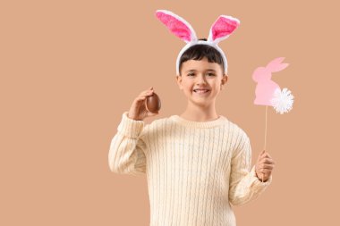 Çikolata yumurtası ve bej arka planda Paskalya için dekorasyonu olan tavşan kulaklı şirin bir çocuk.