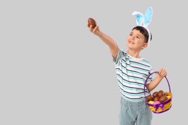 Beyaz arka planda Paskalya için çikolatalı yumurta sepeti tutan tavşan kulaklı şirin bir çocuk.