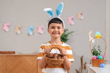 Tavşan kulaklı şirin çocuk evde paskalya için çikolatalı yumurta sepeti tutuyor.