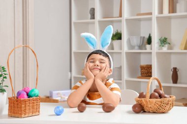 Evde paskalya için çikolata yumurtası sepeti taşıyan tavşan kulaklı şirin bir çocuk.