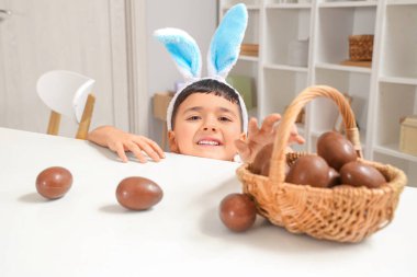 Evde paskalya için çikolata yumurtası sepeti taşıyan tavşan kulaklı şirin bir çocuk.