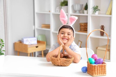 Evde paskalya için çikolata yumurtası sepeti taşıyan tavşan kulaklı şirin bir çocuk.