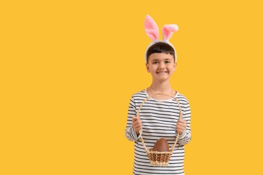 Tavşan kulaklı şirin çocuk sarı arka planda Paskalya için çikolatalı yumurta sepeti tutuyor.