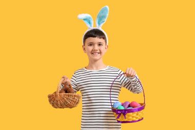 Tavşan kulaklı şirin çocuk sarı arka planda Paskalya yumurtası dolu sepetler tutuyor.