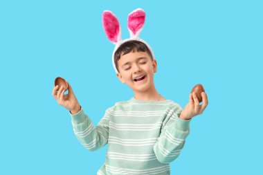 Mavi arka planda Paskalya için çikolatalı yumurtalarla tavşan kulaklı şirin bir çocuk.