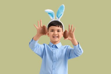 Yeşil arka planda Paskalya için çikolata yumurtalı tavşan kulaklı şirin bir çocuk.