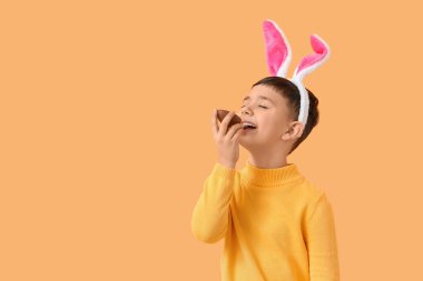 Tavşan kulaklı şirin çocuk turuncu arka planda çikolatalı yumurta yiyor.