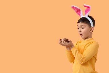 Turuncu arka planda Paskalya için çikolata yumurtalı tavşan kulaklı küçük çocuk.