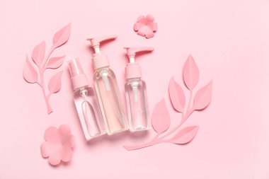 Dispanser ile kozmetik örnekleri, kağıt çiçekler ve pembe arka planda yapraklar