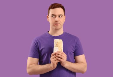 Genç düşünceli bir adam mor arka planda donör kebabı tutuyor.