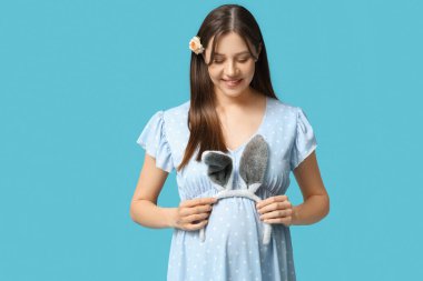 Mavi arka planda tavşan kulaklı güzel hamile bir kadın. Paskalya kutlaması