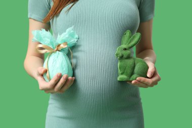 Paskalya hediyesi yumurtası ve yeşil arka planda oyuncak tavşanı olan hamile bir kadın.