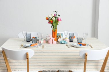 Paskalya için çok güzel bir masa. Beyaz duvara karşı havuç ve çiçeklerle süslenmiş.