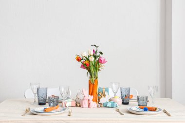 Paskalya için çok güzel bir masa. Beyaz duvara karşı havuç ve çiçeklerle süslenmiş.