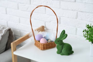 Paskalya yumurtası ve tavşanlı hasır sepet beyaz tuğla duvarın yanında.