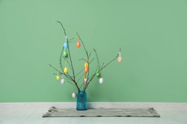 Renk duvarının yanındaki vazoda Paskalya yumurtalarıyla süslenmiş dallar.