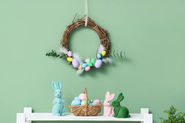 Rafta güzel Paskalya yumurtaları ve tavşanlar ve yeşil duvarda asılı çelenkler.