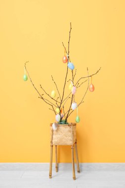 Sarı duvarın yanındaki sepette Paskalya yumurtaları olan güzel dallar.