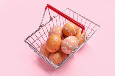 Paskalya yumurtaları pembe arka planda alışveriş sepeti.