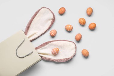 Paskalya tavşanı kulaklı alışveriş çantası ve beyaz arka planda yumurtalar.