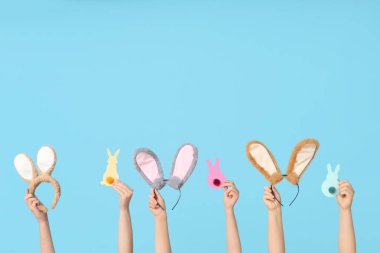 Paskalya tavşanı kulaklıklarını tutan kadın eller ve mavi arka planda kağıt tavşanlar.