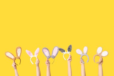 Sarı arka planda Paskalya tavşanı kulaklığı tutan kadın eller.