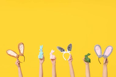 Paskalya tavşanı kulaklıklarını tutan kadın elleri ve sarı arka planda oyuncak tavşanlar.