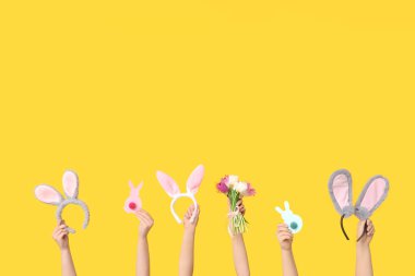 Paskalya tavşanı kulaklıkları tutan kadın eller. Sarı arka planda kağıt tavşanlar ve laleler.