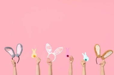 Paskalya tavşanı kulaklıklarını tutan kadın eller ve pembe arka planda kağıt tavşanlar.
