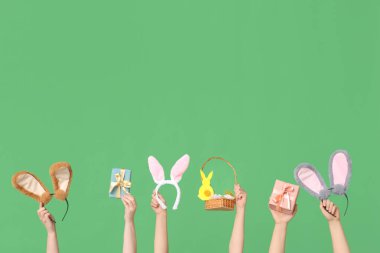 Paskalya tavşanı kulaklığı takan, hediye kutuları ve yeşil arka planda sepeti olan kadın elleri.