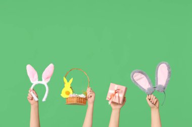 Paskalya tavşanı kulaklığı takan, yeşil arka planda hediye kutusu ve sepeti olan kadın elleri.