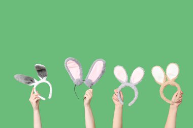 Yeşil arka planda Paskalya tavşanı kulaklığı tutan kadın elleri.