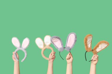 Yeşil arka planda Paskalya tavşanı kulaklığı tutan kadın elleri.