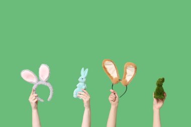 Paskalya tavşanı kulaklıkları ve yeşil arka planda oyuncak tavşanları tutan kadın elleri.
