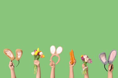 Paskalya tavşanı kulaklıklı, havuçlu ve yeşil arka planda laleli kadın elleri.