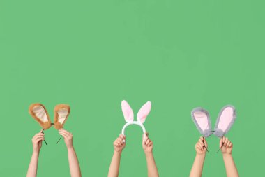 Yeşil arka planda Paskalya tavşanı kulaklığı tutan kadın elleri.