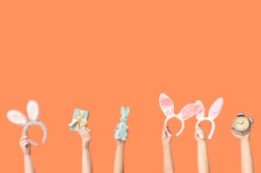 Paskalya tavşanı kulaklıklı hediye kutusu ve turuncu arka planda çalar saati olan kadın eller.