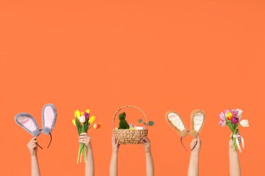 Paskalya tavşanı kulaklıklı, sepetli ve turuncu arka planda laleli kadın elleri.