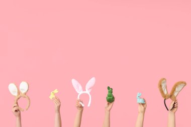 Paskalya tavşanı kulaklıklarını tutan kadın elleri ve pembe arka planda oyuncak tavşanlar.