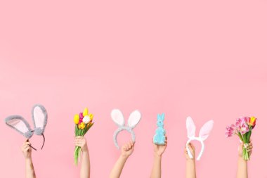 Paskalya tavşanı kulaklıklı, oyuncak tavşanlı ve pembe arka planda laleli kadın elleri.