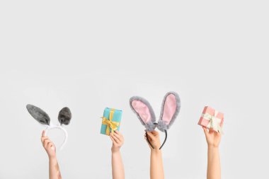 Paskalya tavşanı kulaklıklarını tutan kadın elleri ve beyaz arka planda hediye kutuları.