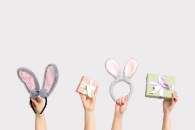 Paskalya tavşanı kulaklıklarını tutan kadın elleri ve beyaz arka planda hediye kutuları.