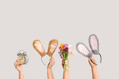 Paskalya tavşanı kulaklıkları tutan kadın eller. Alarmlı bantlar ve beyaz arka planda laleler.